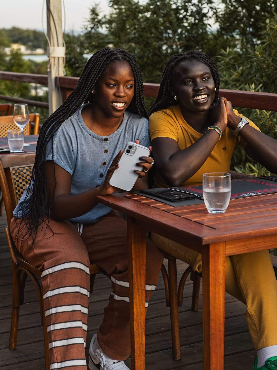 Two friends compare places on a single phone at a terrace table